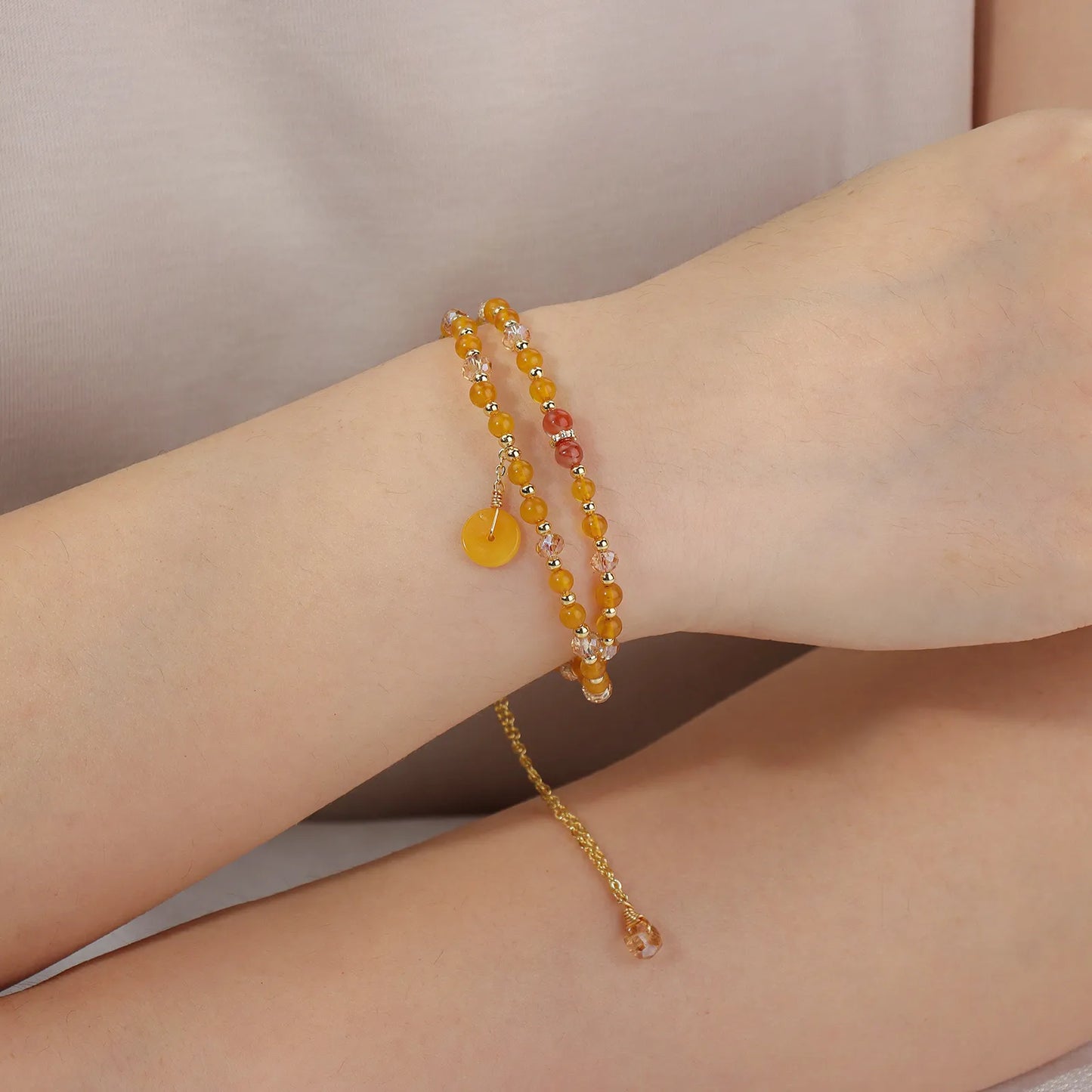 A double - layered beaded bracelet with yellow and light pink beads and a gold - tone disc charm.