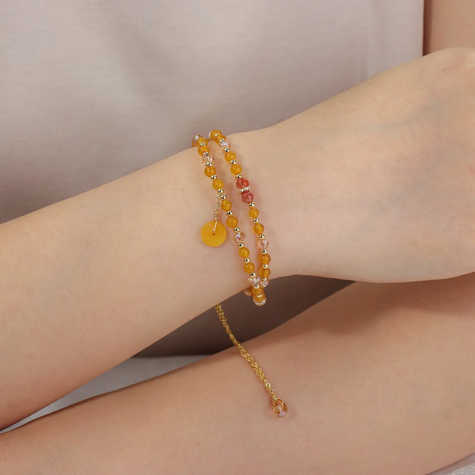 A double - layered beaded bracelet with yellow and light pink beads and a gold - tone disc charm.