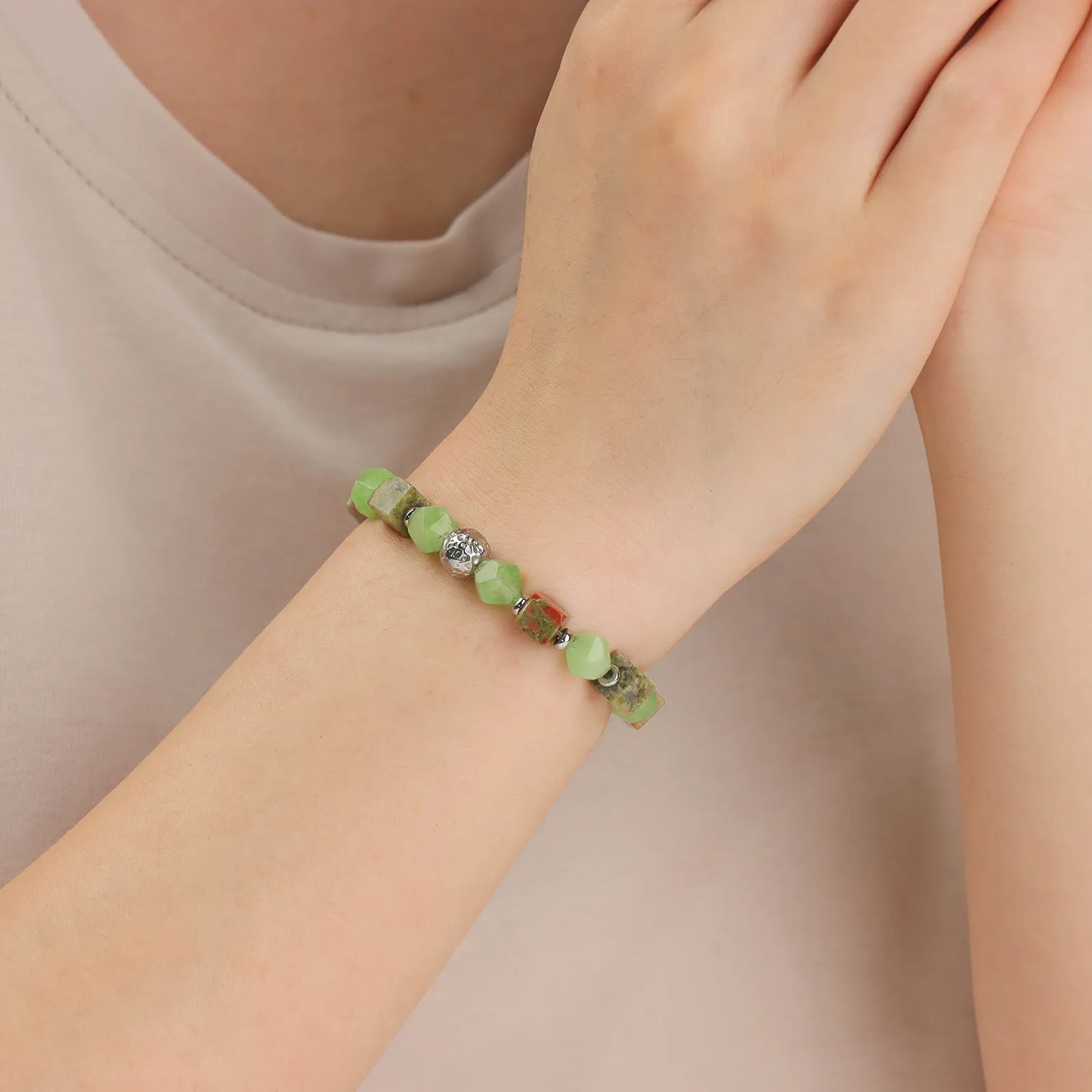 A beaded bracelet with green stones and metallic - colored cubes.