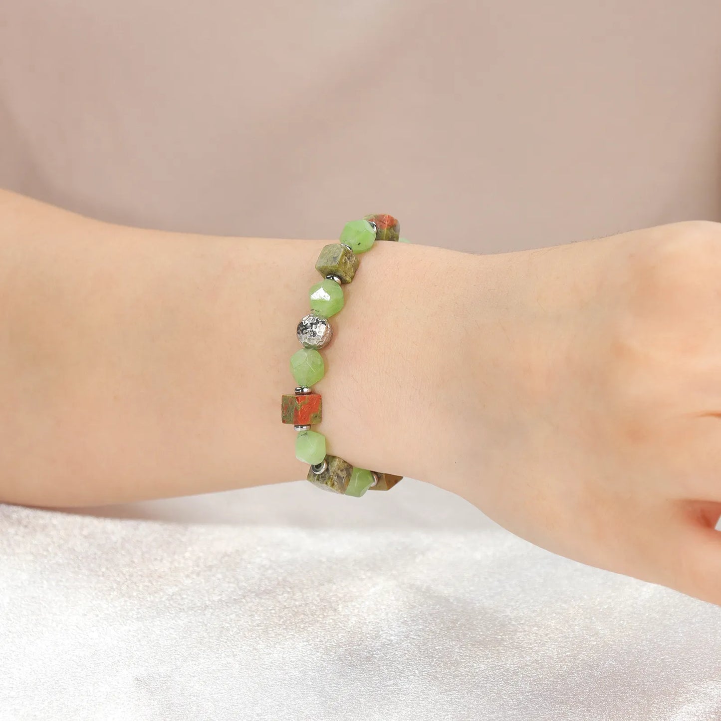 A beaded bracelet with green stones and metallic - colored cubes.