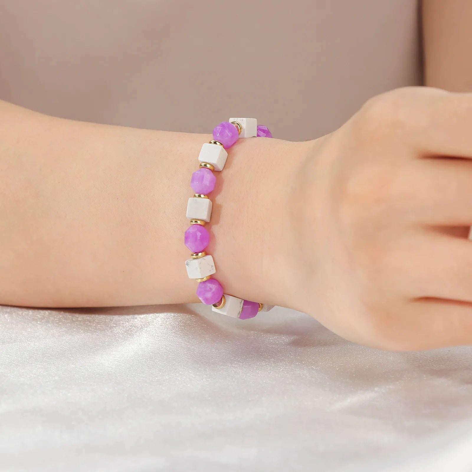 A beaded bracelet made of purple stone and white beads with gold accents.