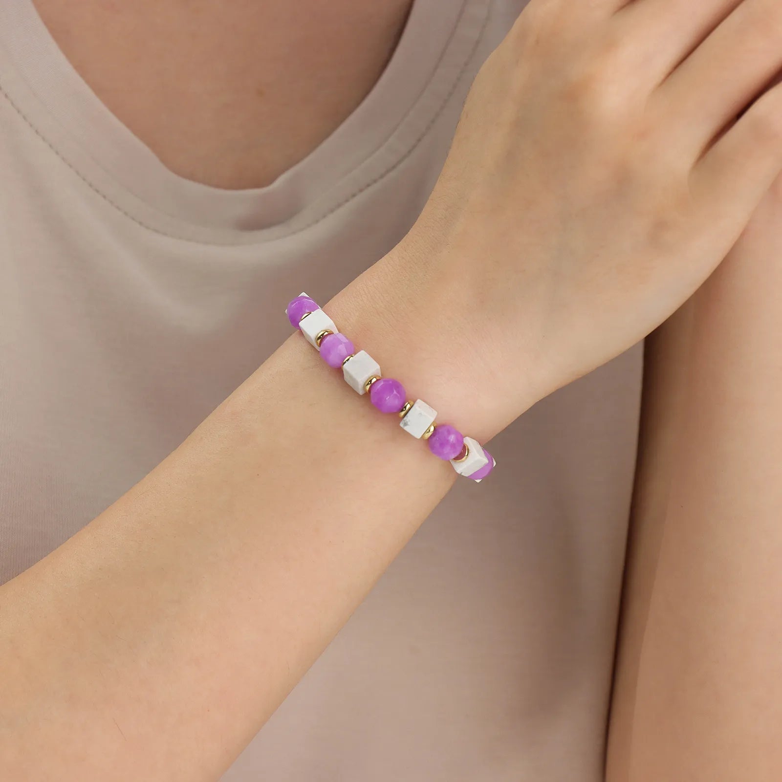 A beaded bracelet made of purple stone and white beads with gold accents.