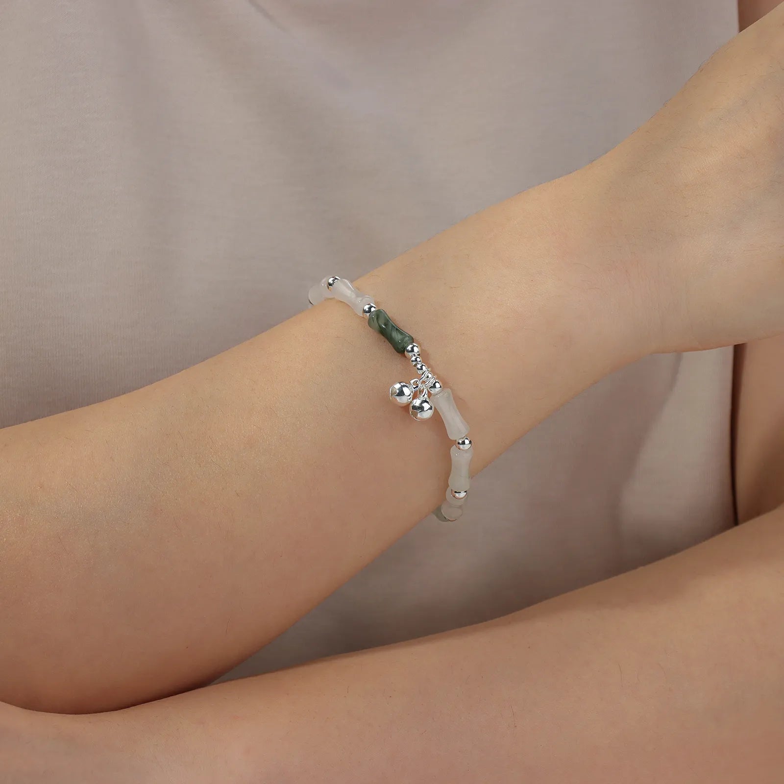 Bead chain bracelet with bamboo - shaped stones and silver bells, showing elegant oriental style.